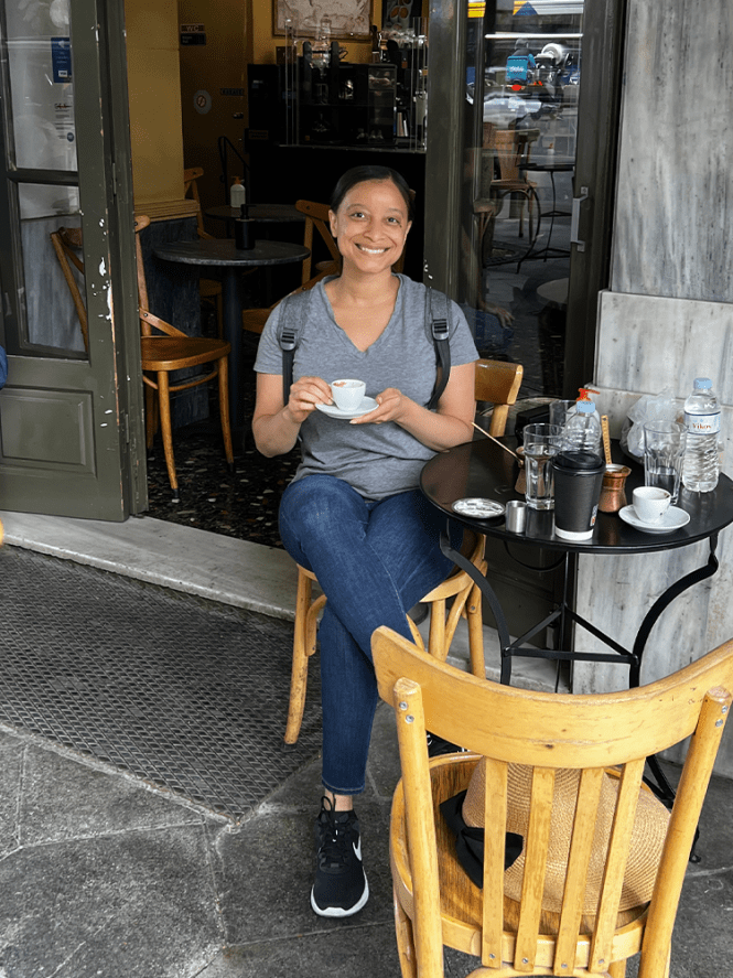 Photo of Antoinette sitting outside a coffee shop holding a cup of Greek coffee in Athens Greeece.